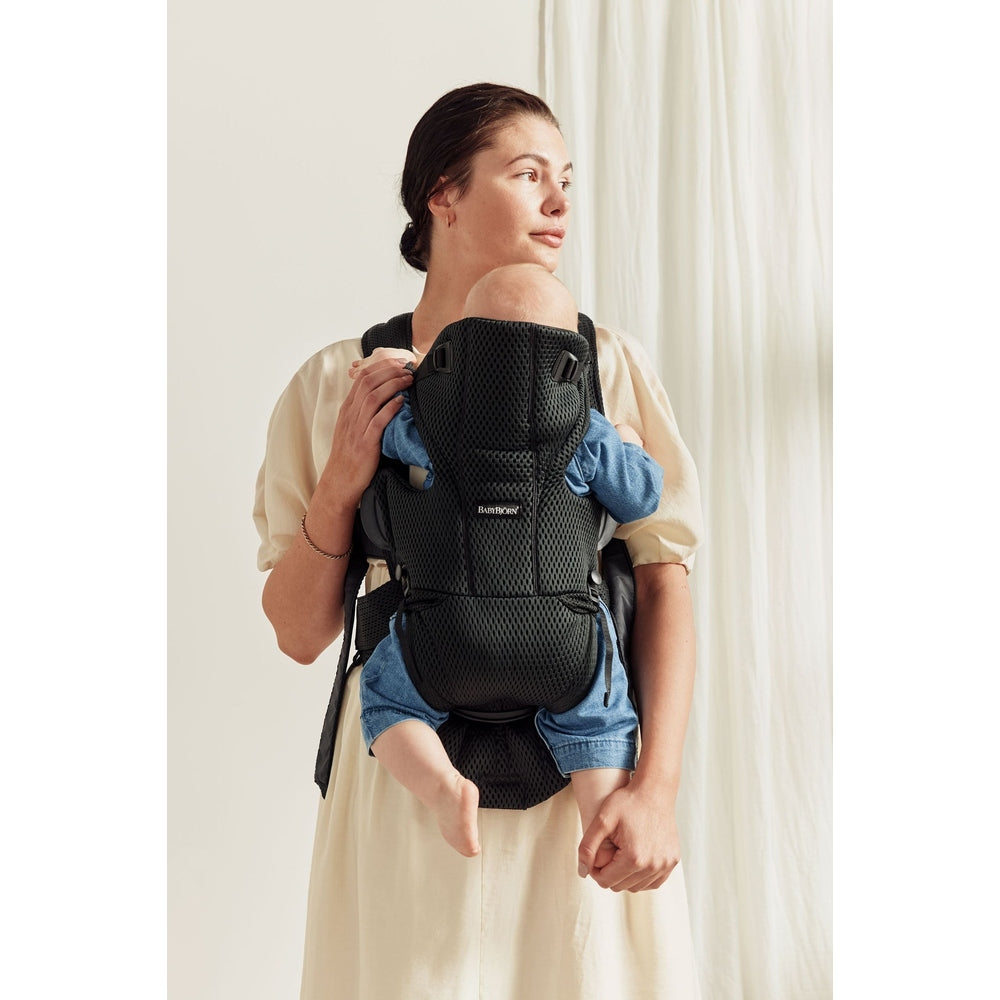 BabyBjörn Baby Carrier Free in black mesh worn by mom with baby snug against her chest, hands-free support.