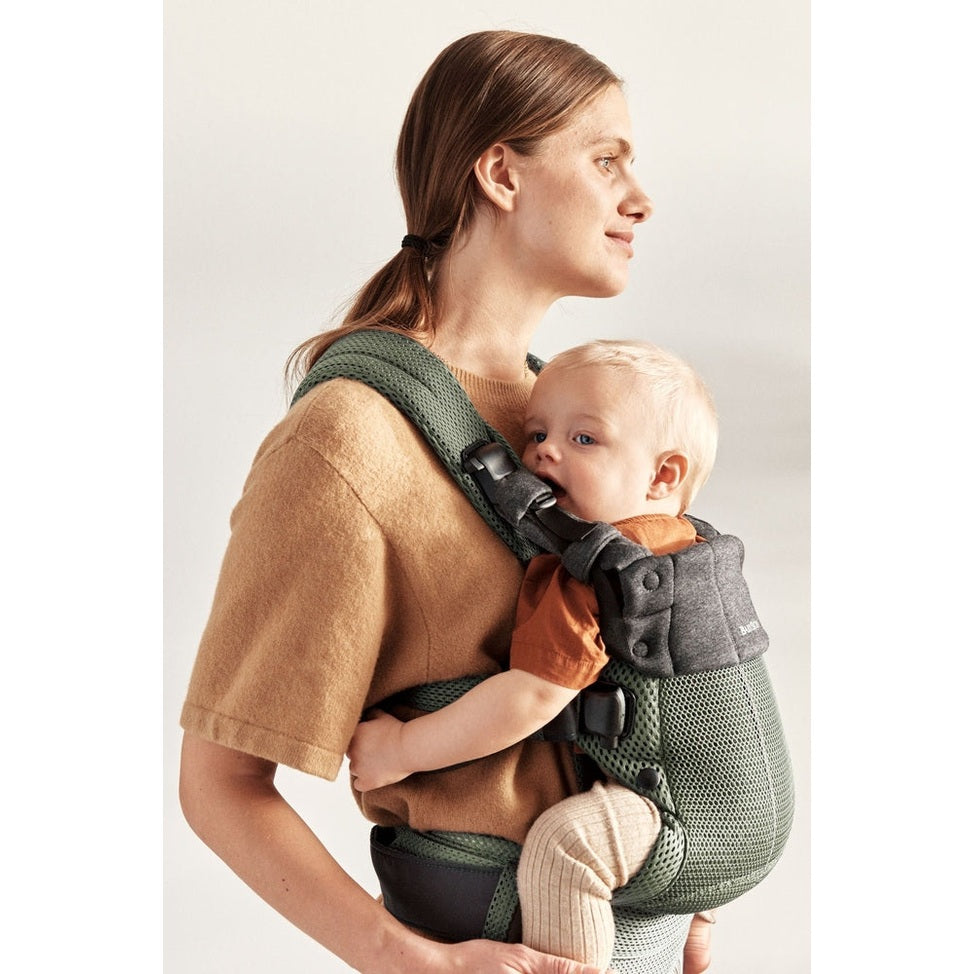 BabyBjörn Harmony baby carrier in green mesh worn by mother with buckled straps, baby facing chest.