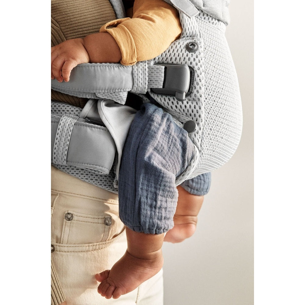 BabyBjörn Harmony baby carrier, gray mesh with padded straps, worn by caregiver as baby’s legs dangle securely.
