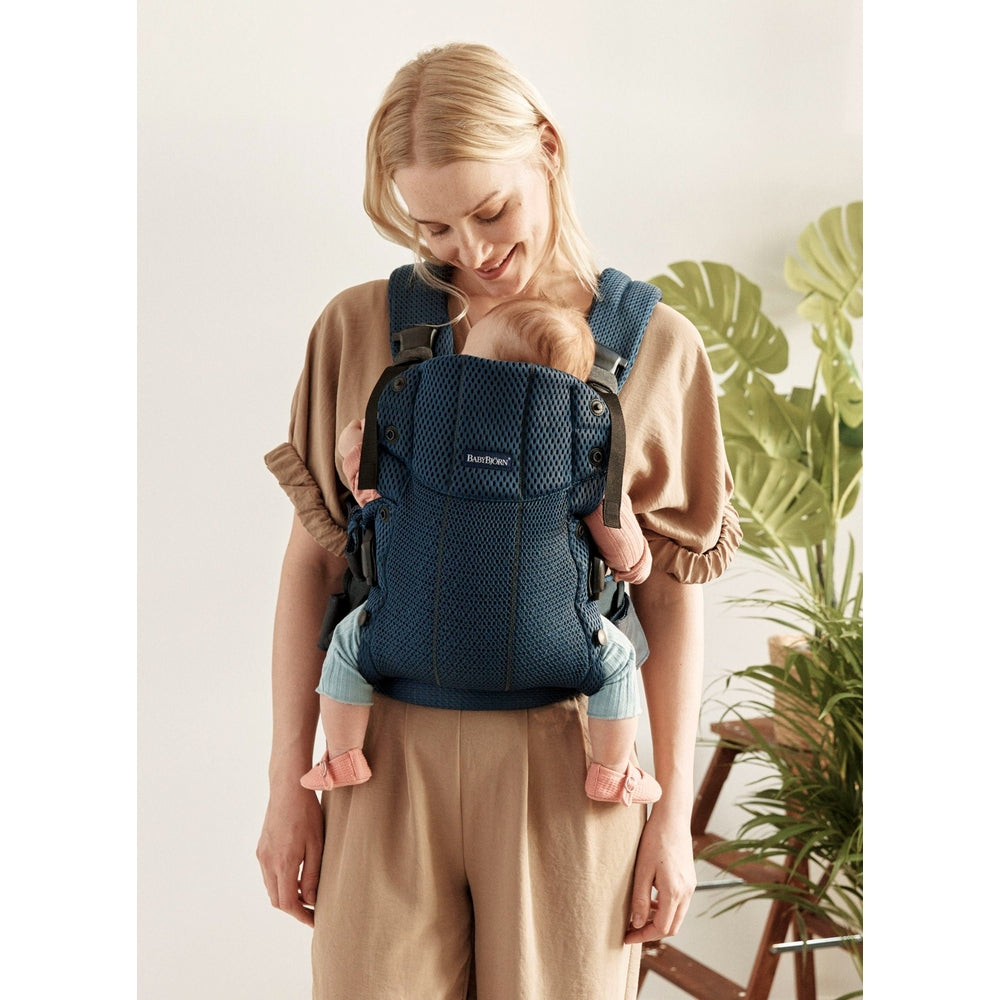 Mother wearing BabyBjörn Harmony baby carrier in navy blue, baby snug against her chest with secure shoulder straps.