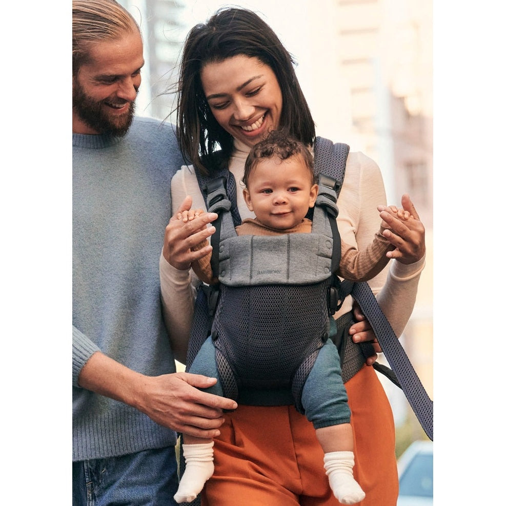 BabyBjörn Harmony baby carrier in gray, worn by a smiling mom with baby securely in an ergonomic front carry.