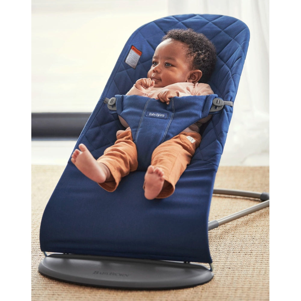 BabyBjörn Bouncer Bliss in navy blue fabric; baby securely buckled in a 5-point harness while reclining in the rocker.