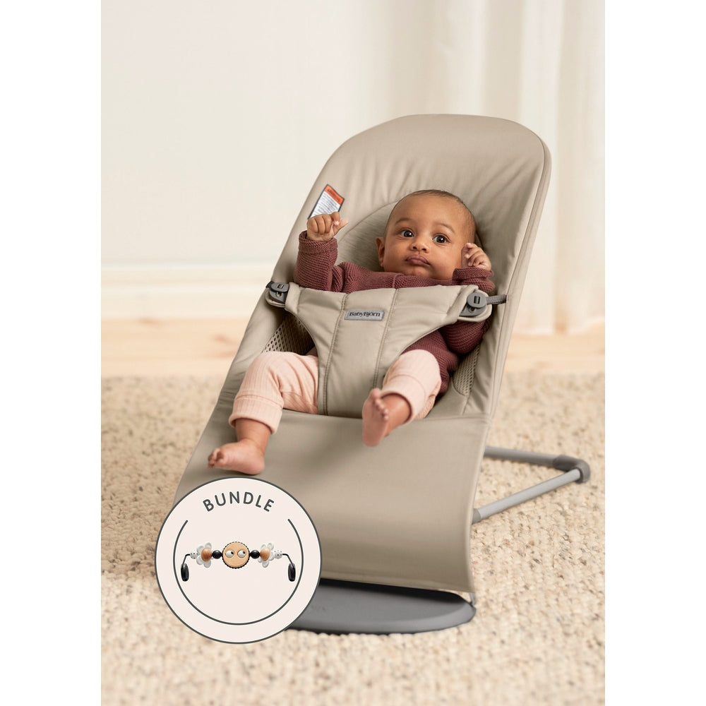 BabyBjörn Bouncer Bliss in beige, baby secured in the reclined harness on a sturdy stand, bundle badge visible.
