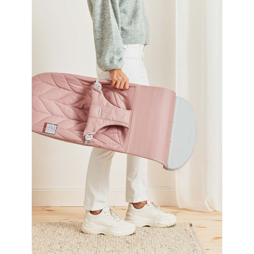 BabyBjörn Bouncer Bliss pink, being carried by a person with the folded seat and carry handle visible.