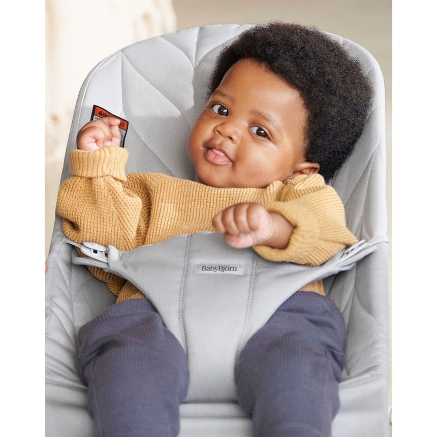BabyBjörn Bouncer Bliss in gray; infant in mustard sweater sits settled, securely strapped in.