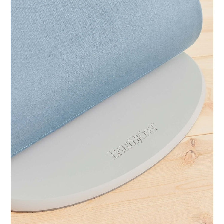 BabyBjörn Bouncer Bliss blue fabric seat atop a gray circular base on a wooden floor.