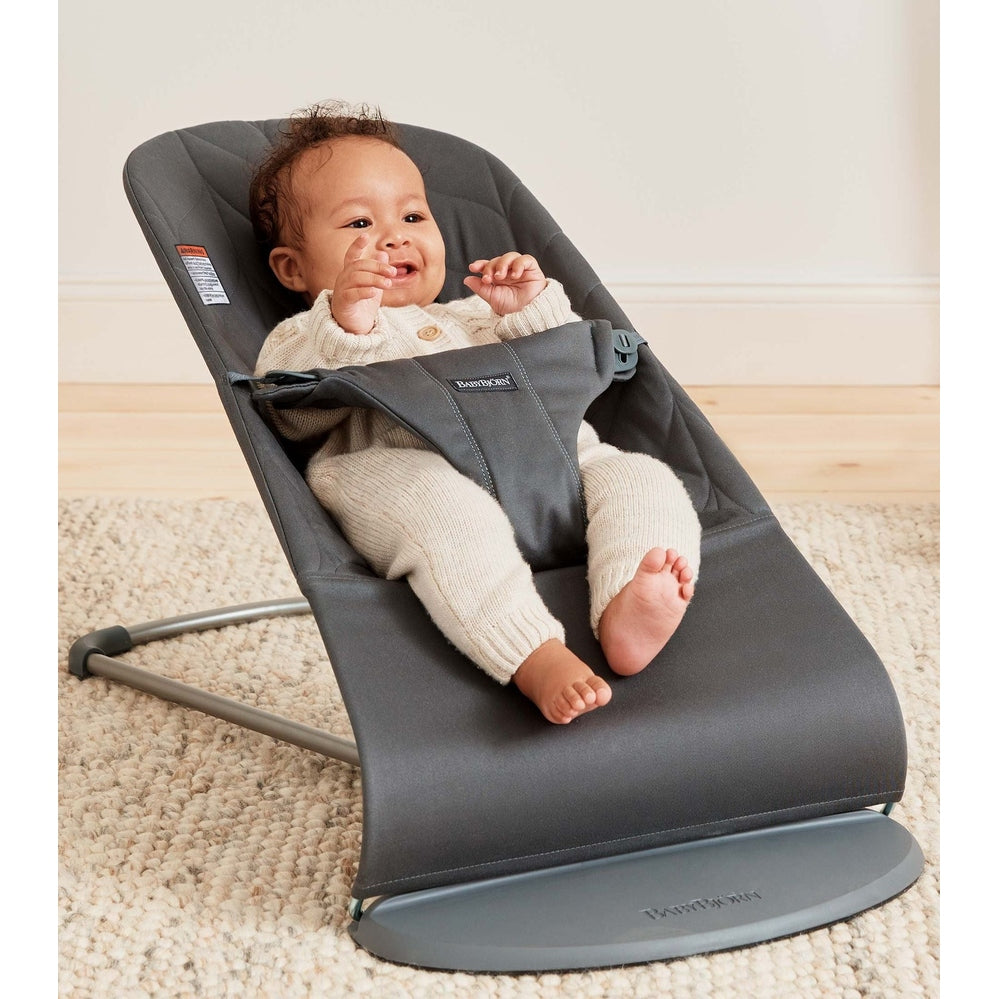 BabyBjörn Bouncer Bliss gray fabric, baby buckled and smiling in the reclined rocker.