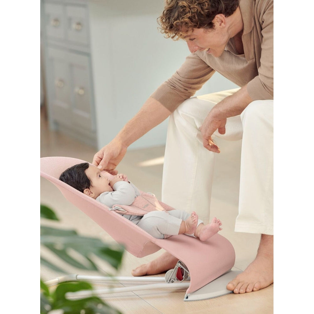 BabyBjörn Bouncer Bliss pink infant bouncer; parent softly touches baby’s face as infant reclines.