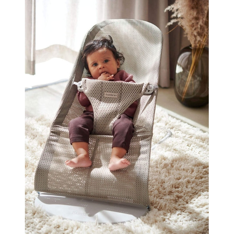 BabyBjörn Bouncer Bliss gray mesh infant bouncer; baby sits securely with feet dangling in a cozy living room.