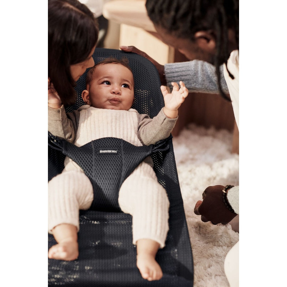 BabyBjörn Bouncer Bliss in breathable mesh, baby smiles with arms out as caregivers lean in.