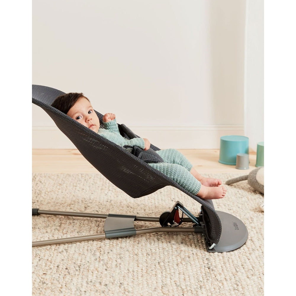 BabyBjörn Bouncer Bliss in dark gray mesh with metal frame; baby reclines in the rocker on a cream carpet.