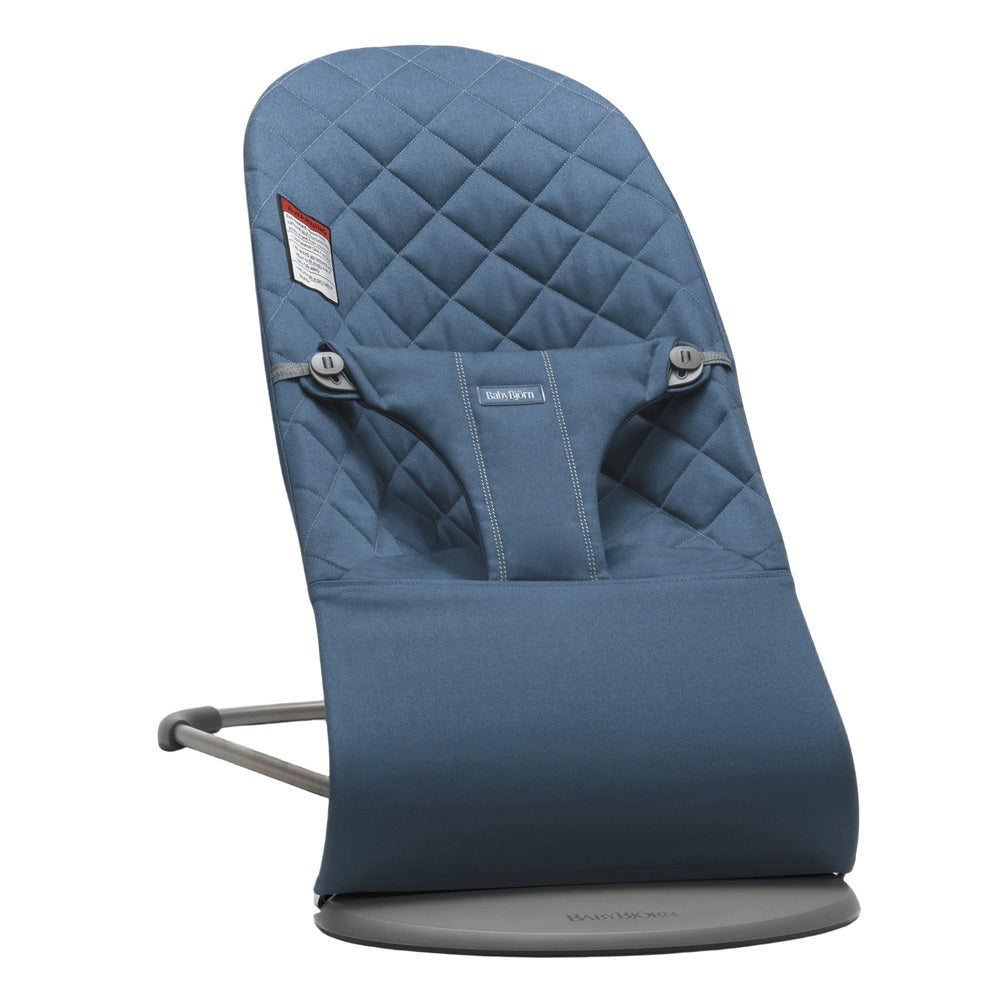 BabyBjörn Bouncer Bliss in blue quilted fabric, with secured harness, resting on a round gray base.