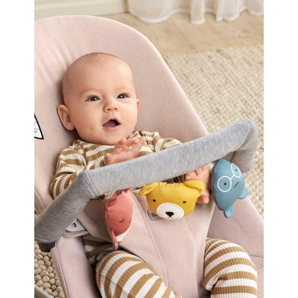 BabyBjörn Baby Bouncer Toy: soft pink seat with gray bar as baby reaches colorful plush toys.