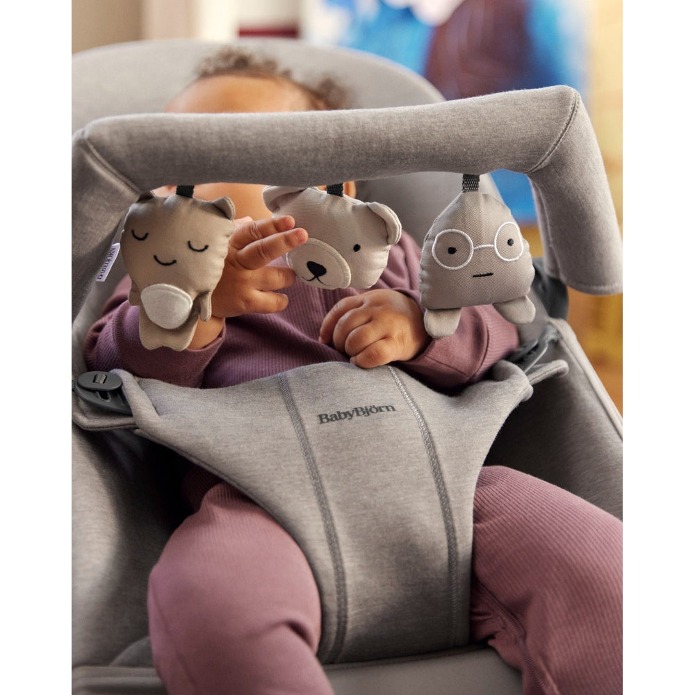 BabyBjörn Bouncer Toy in gray with hanging plush animals; baby reaches for the toys while seated.