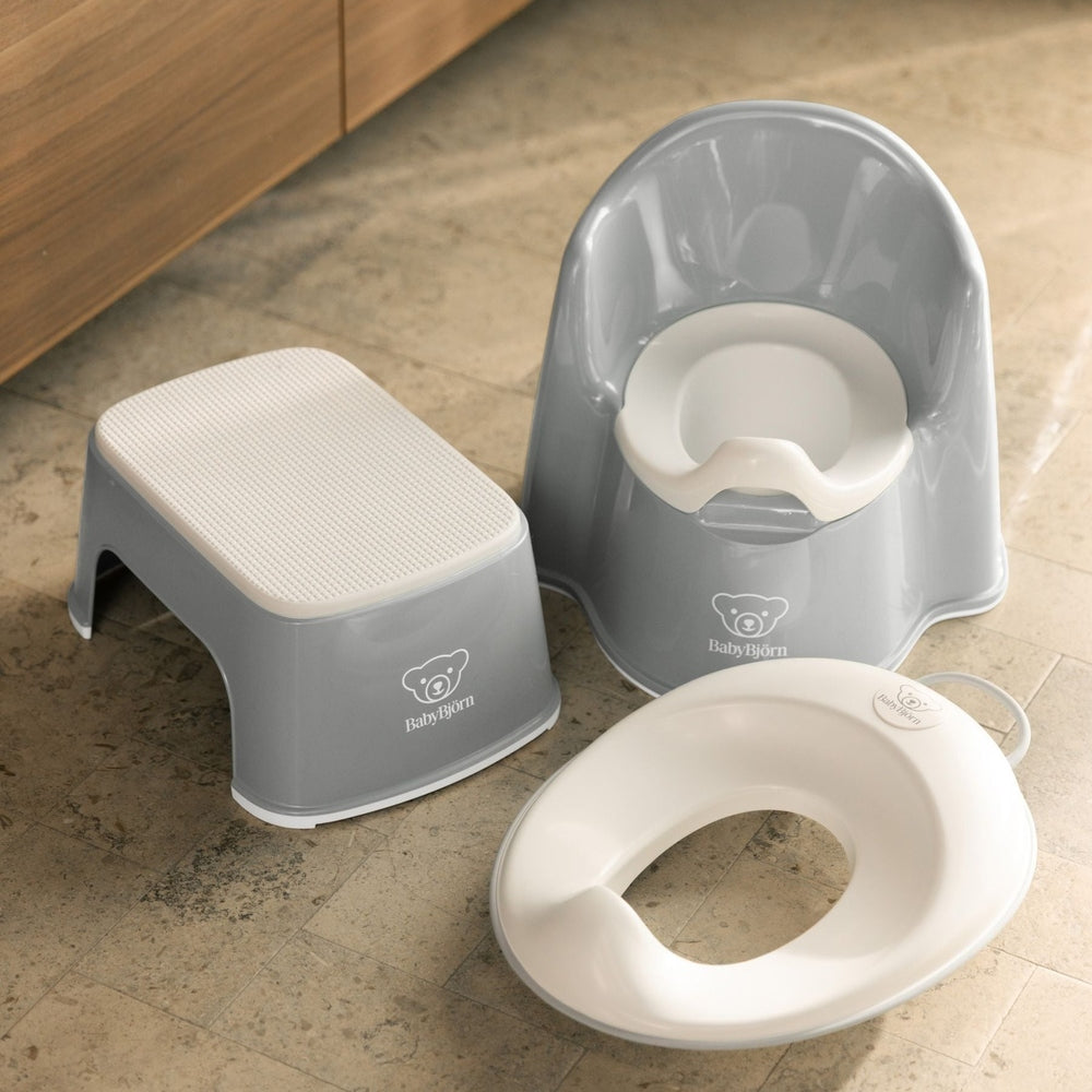 BabyBjörn Potty Chair set in gray with a textured step stool and white seat, shown with a toddler stepping up to use.