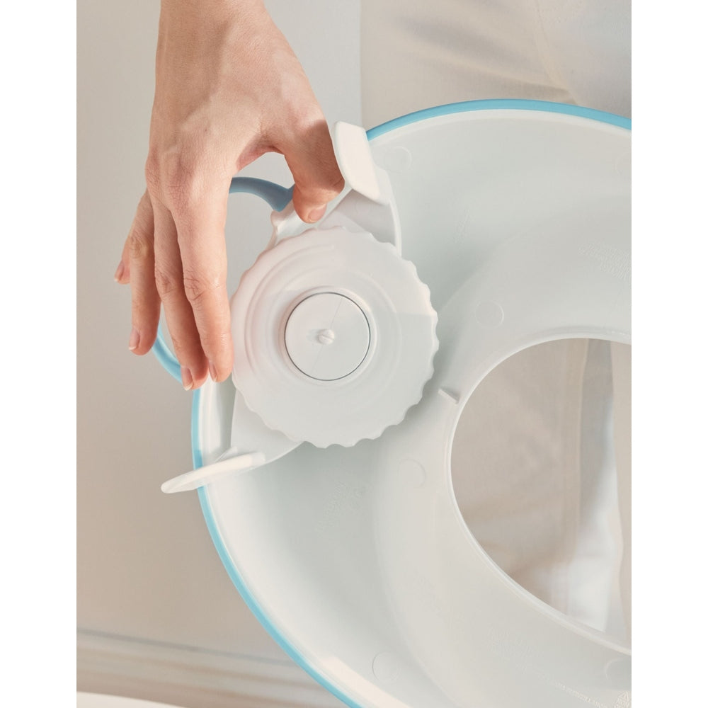 BabyBjörn Toilet Trainer, blue/white, as a parent turns the adjustment dial to secure it.