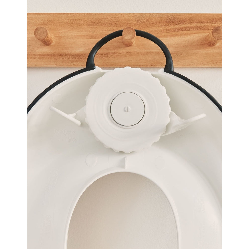 BabyBjörn Toilet Trainer, white, mounted to a toilet with a large adjustable dial for easy fit.