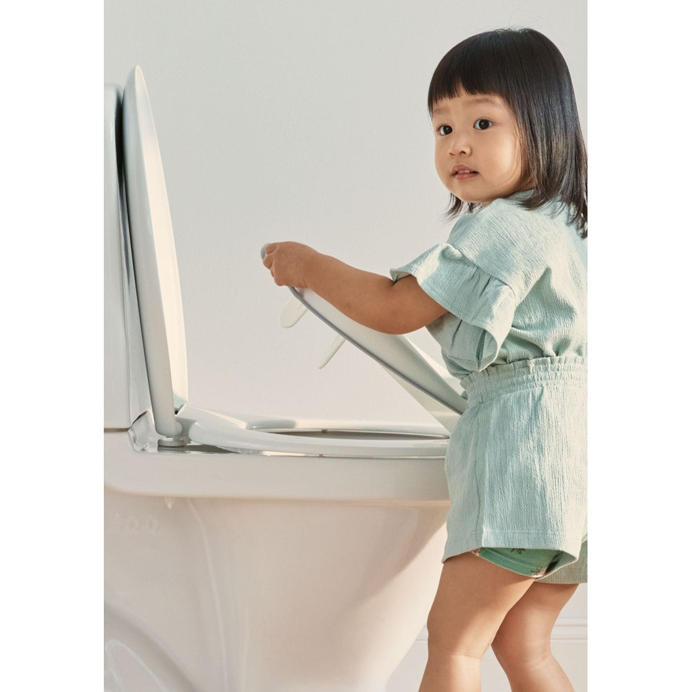 BABY BJÖRN Toilet Trainer in mint green as a toddler lifts the training seat onto a toilet.