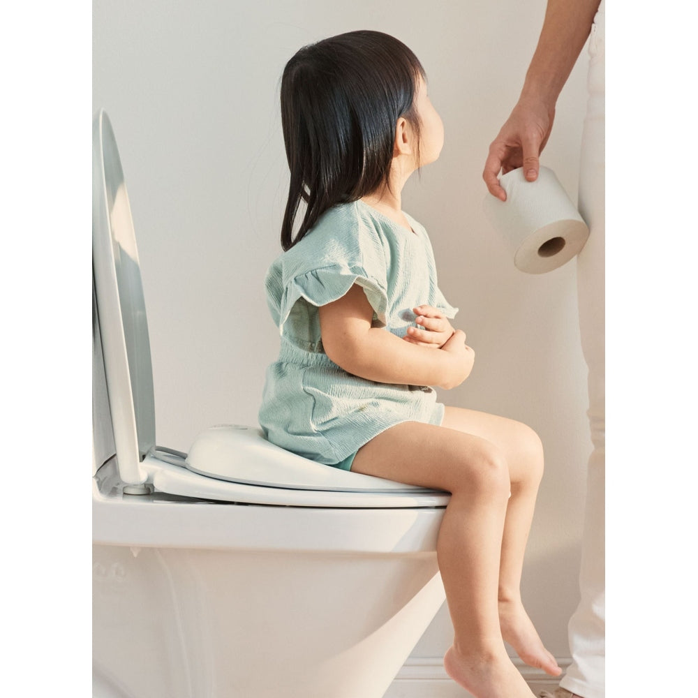 BabyBjörn Toilet Trainer in green; a child sits on the toilet as an adult holds toilet paper.