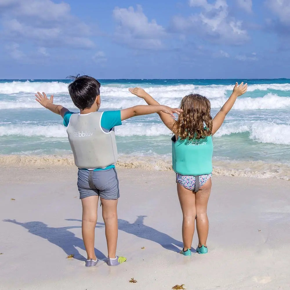 BBLUV Naj Evolutive Neoprene Swim Vest Aqua; kids on the beach raise arms to show buoyant, secure neoprene fit.