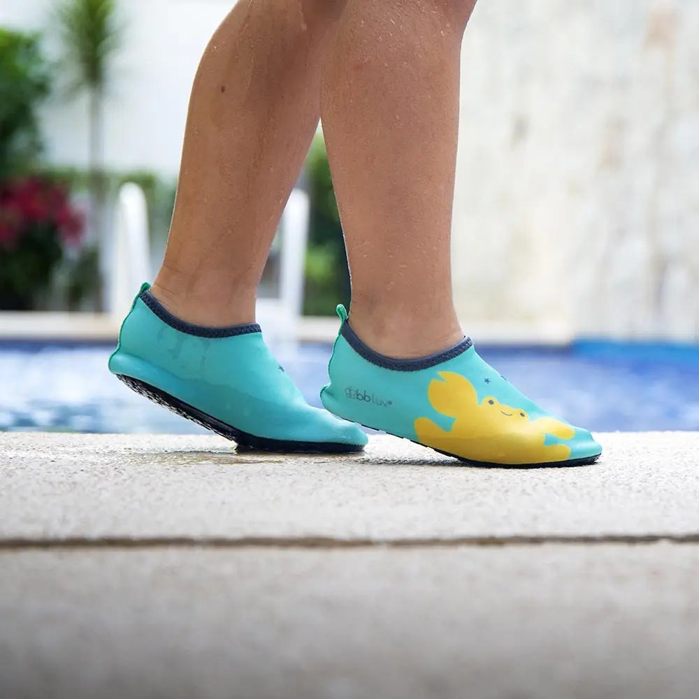 BBLUV Shooz Neoprene Protective Water Shoes Aqua; toddler walks along the pool edge in aqua shoes with yellow duck print.