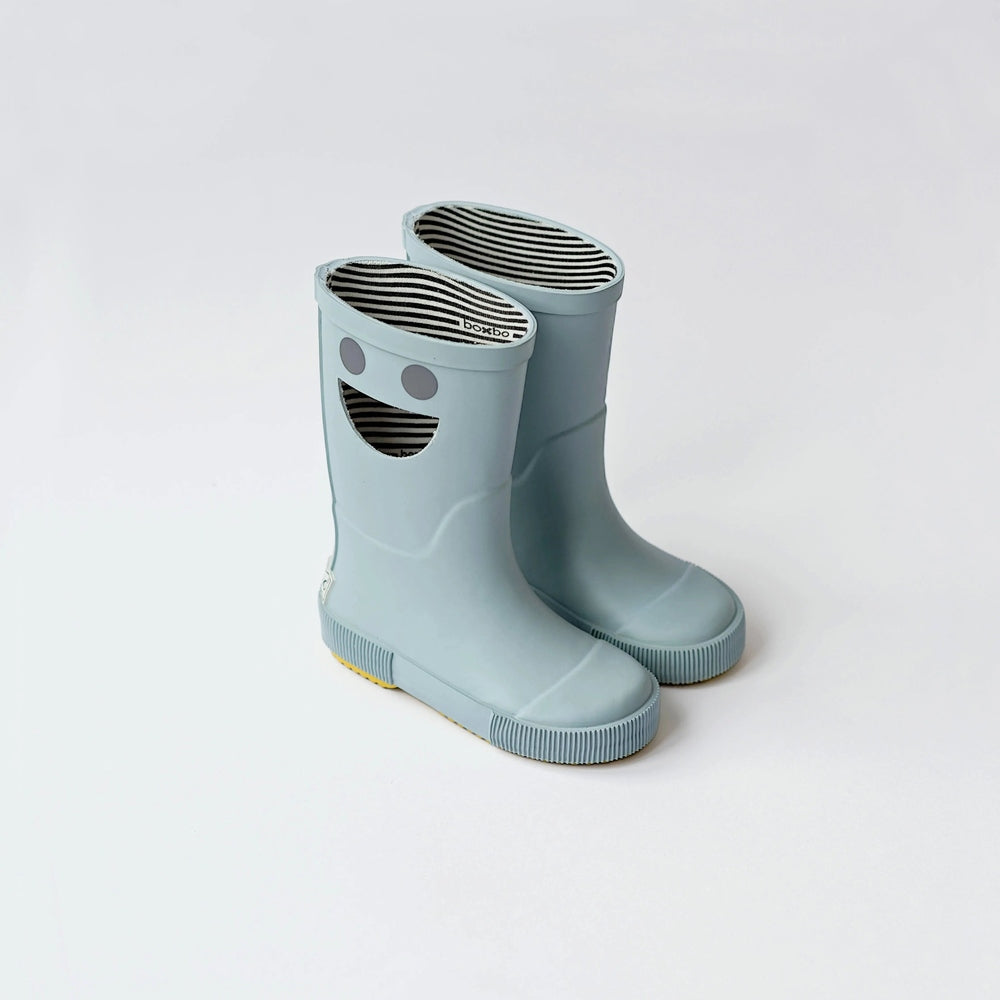 Boxbo Wistiti Rainboots Platine; light blue rubber boots with striped lining and a smiling face, pair standing together.