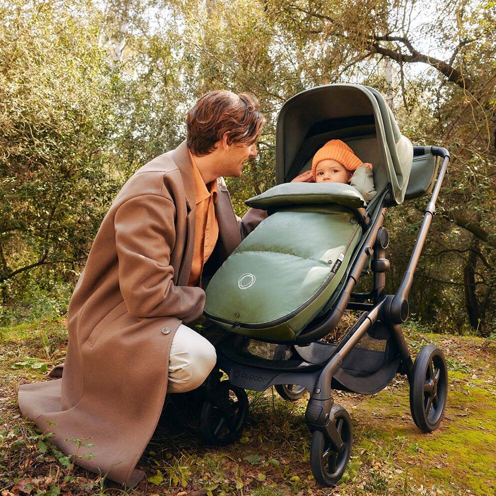 Bugaboo THERMOLITE® Performance Footmuff in green attached to a stroller during a cozy winter stroll with a baby.