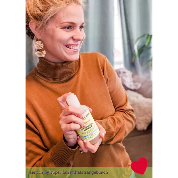 California Baby Everywhere Spritzer Eucalyptus 6.5 oz bottle held by smiling woman in a brown turtleneck