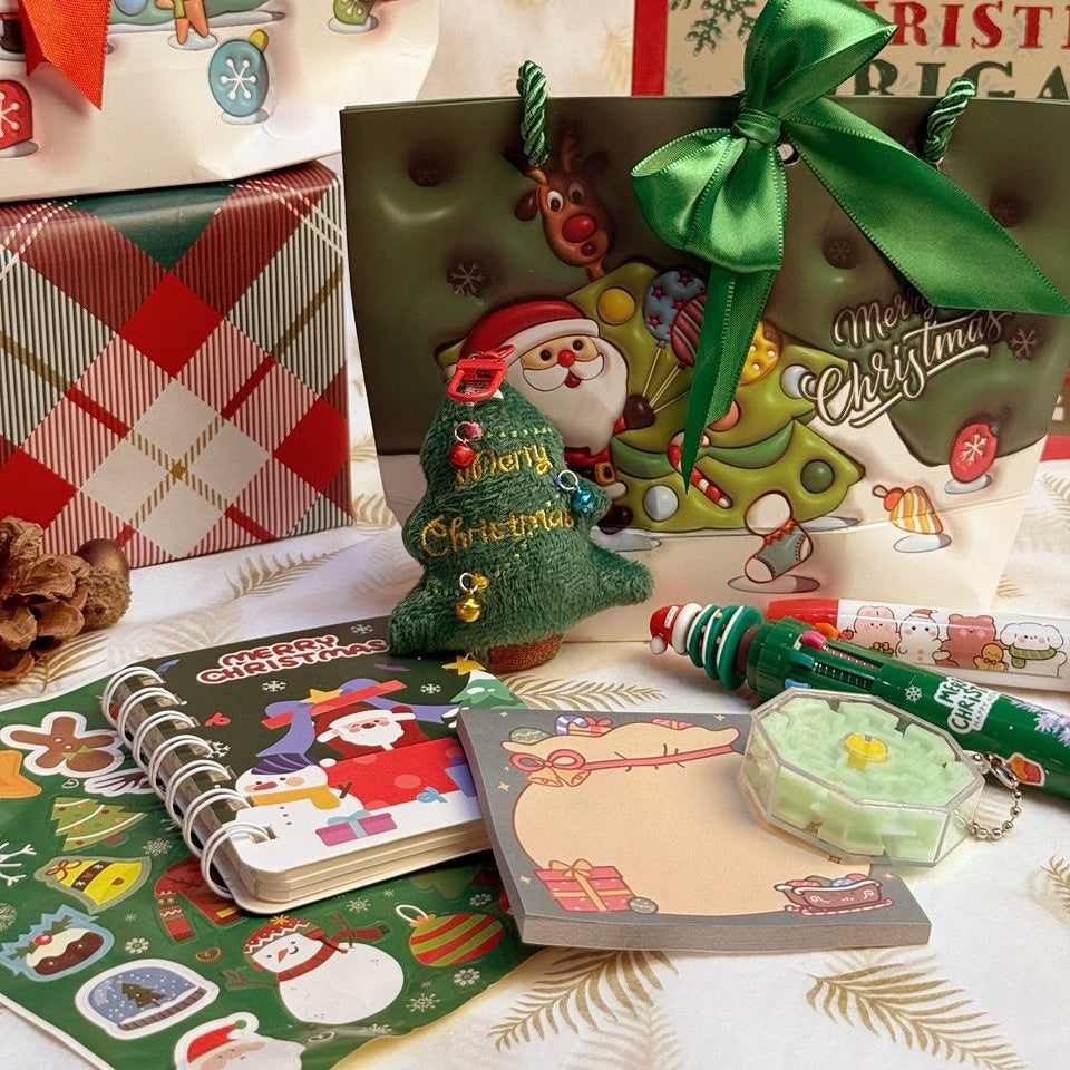 Christmas Stationery Gift Bag by baby enRoute in a festive scene with notebook, stickers, pencil, and a green ribboned bag.