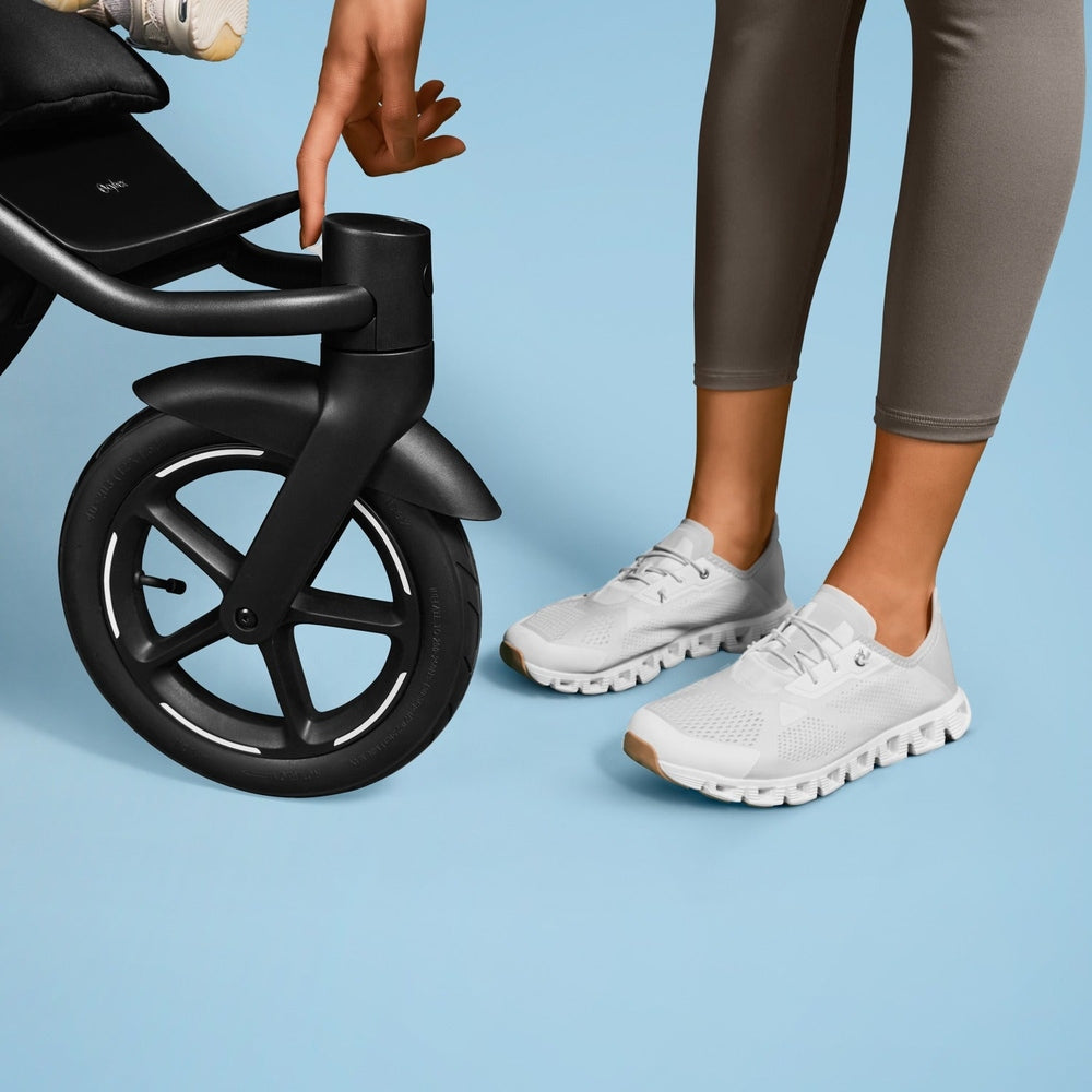 Cybex Avi Spin All Terrain Stroller in black, parent adjusting the front handle near the large wheel.