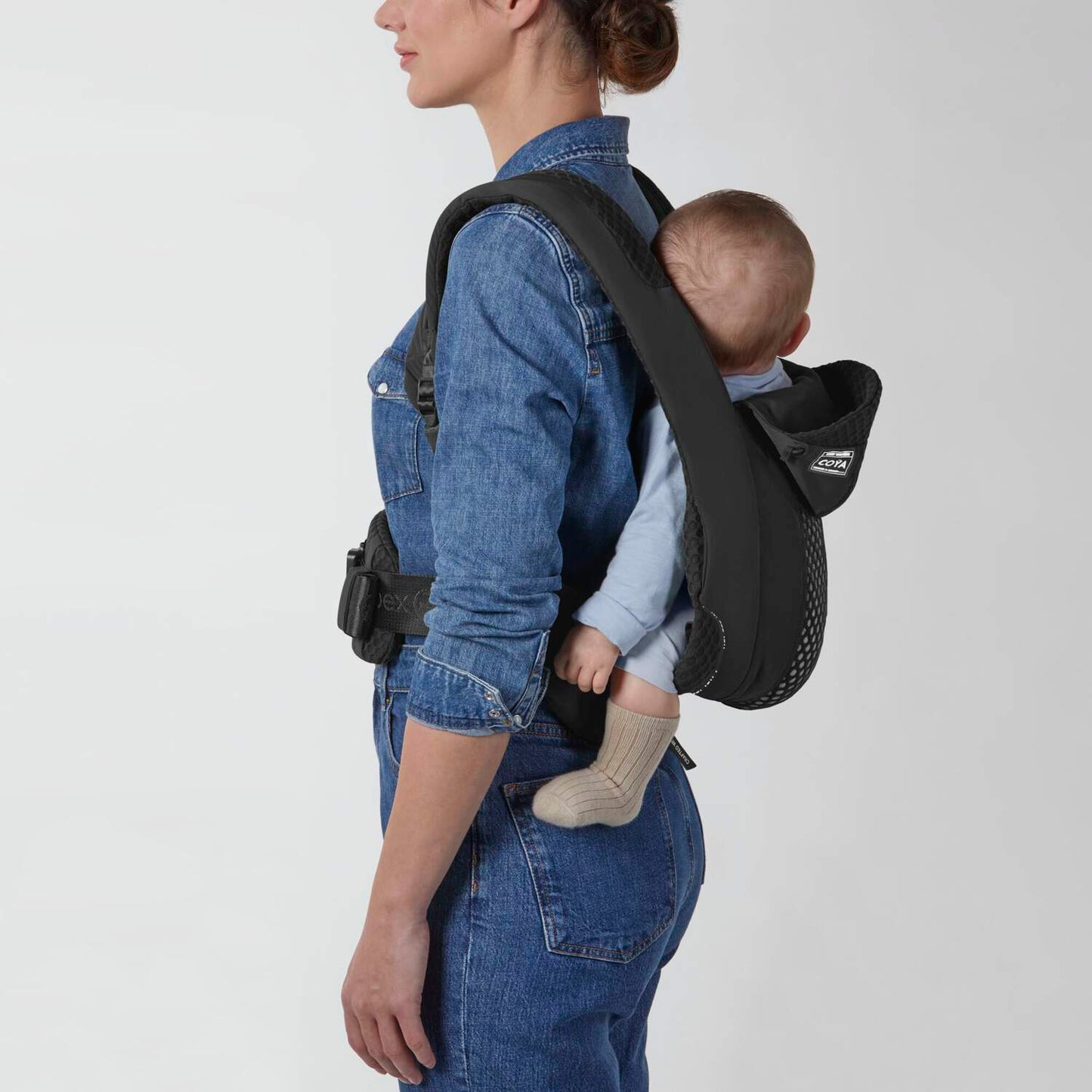 Cybex Coya baby carrier in black worn on back by parent with infant.