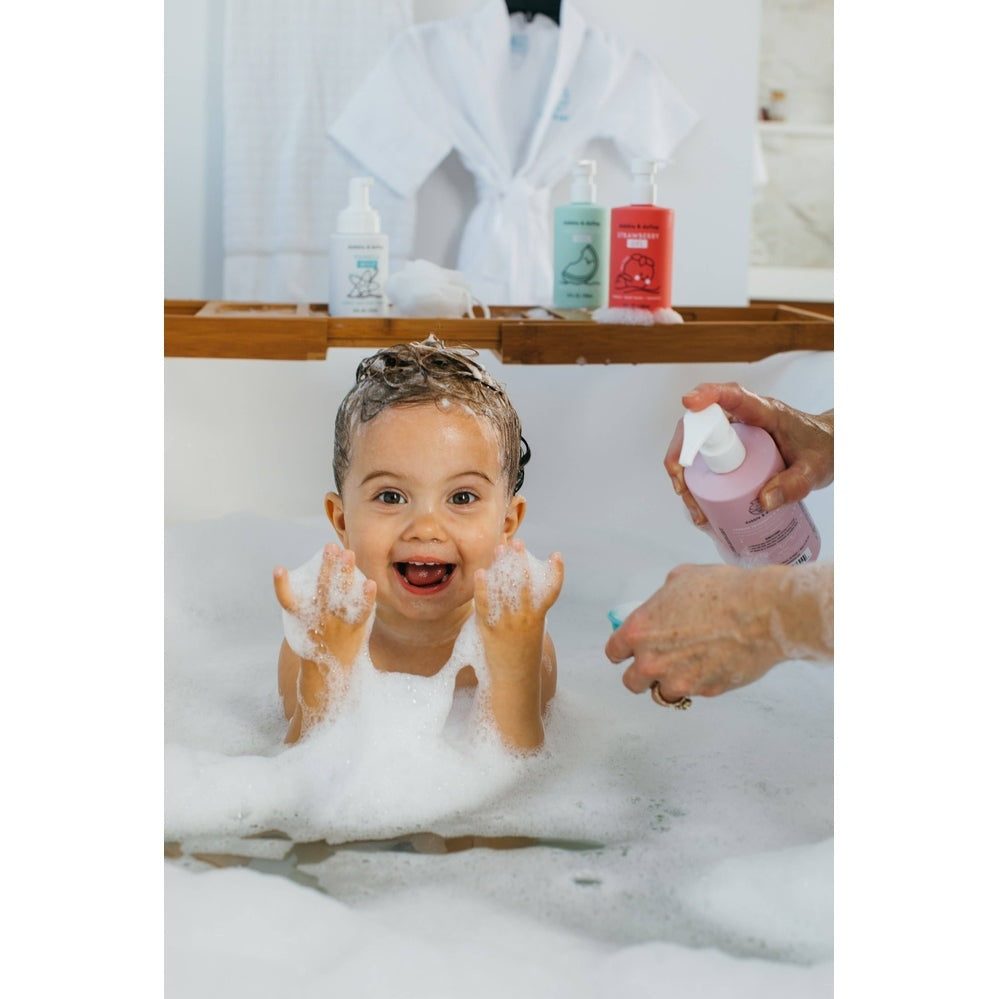 Dabble & Dollop All-Natural Shampoo, Body Wash & Bubbles Coconut: child joyful in foamy bath as caregiver pours coconut wash.