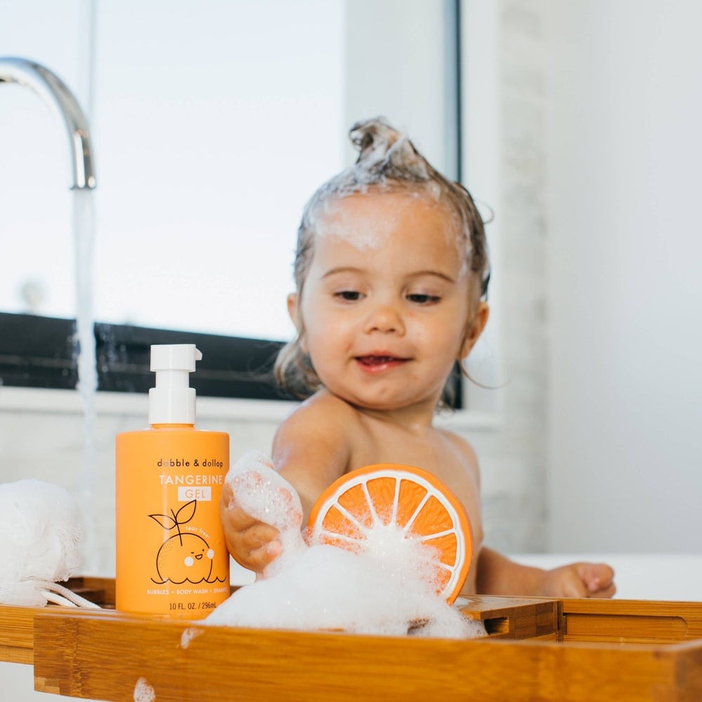 Dabble & Dollop All-Natural Shampoo, Body Wash & Bubbles Tangerine bottle sits beside foamy bath as a baby plays.