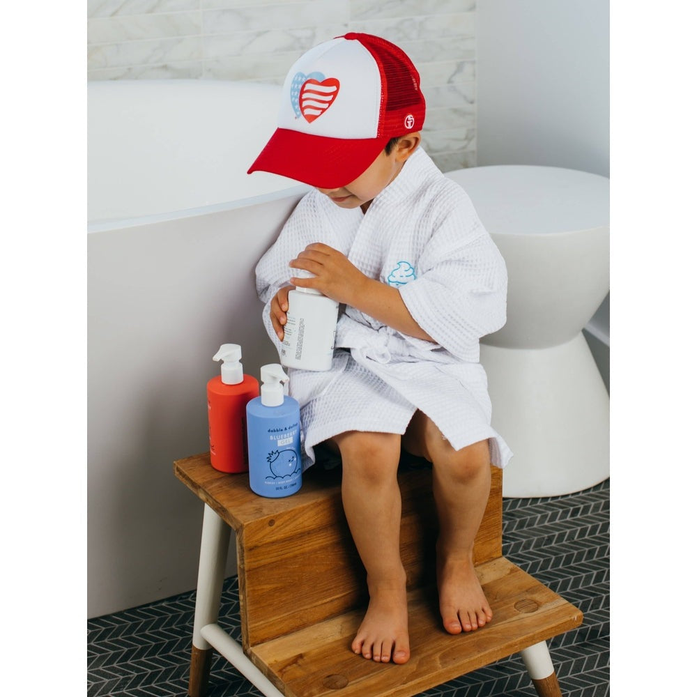 Dabble & Dollop All-Natural Blueberry Shampoo, Body Wash & Bubbles set; child in robe holds a bottle beside orange and blue pumps.