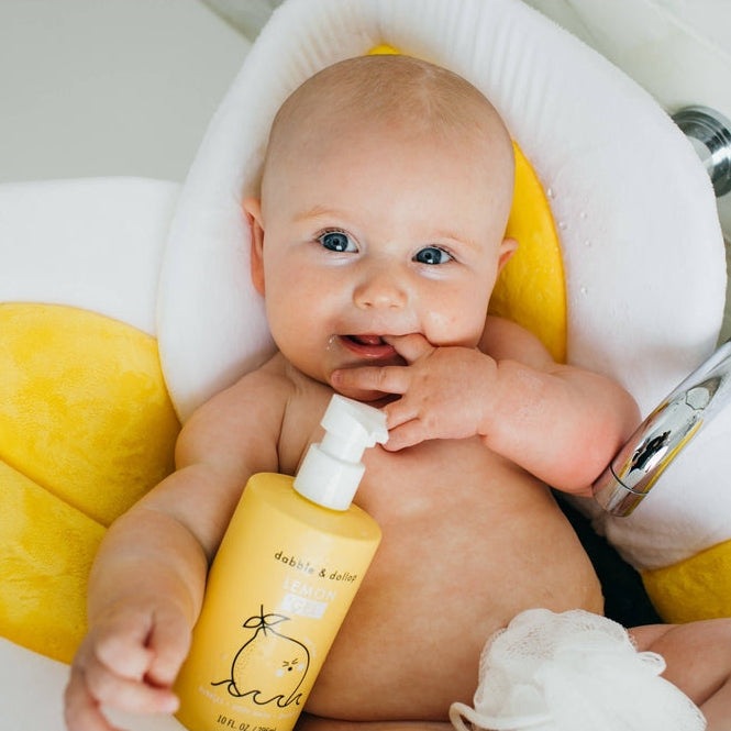 Baby holding a yellow bottle with a white pump in a bathtub.