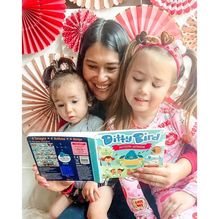 Ditty Bird Sound Book Action Songs USB-C Rechargeable; mother and two kids read it together amid festive decor.