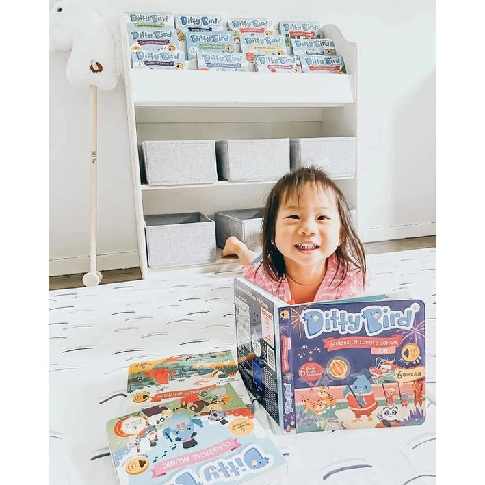 Ditty Bird Sound Book Chinese Songs USB-C Rechargeable toy; cheerful child sits on a playmat with the colorful packaging on shelves.