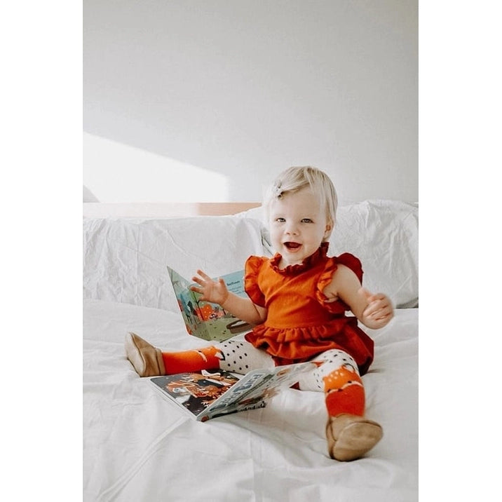 DITTY BIRD Sound Book Christmas Songs USB-C Rechargeable; baby in red sits on a bed reading and turning pages.