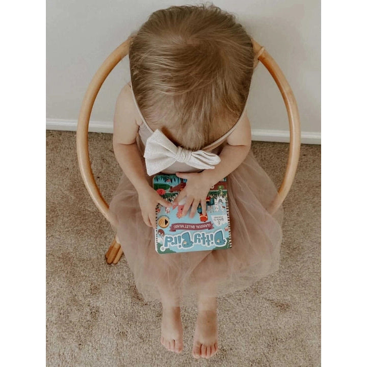 Ditty Bird Sound Book Classical Ballet Music USB-C Rechargeable; toddler in a pink ballet tutu sits in a wooden hoop chair reading the book.