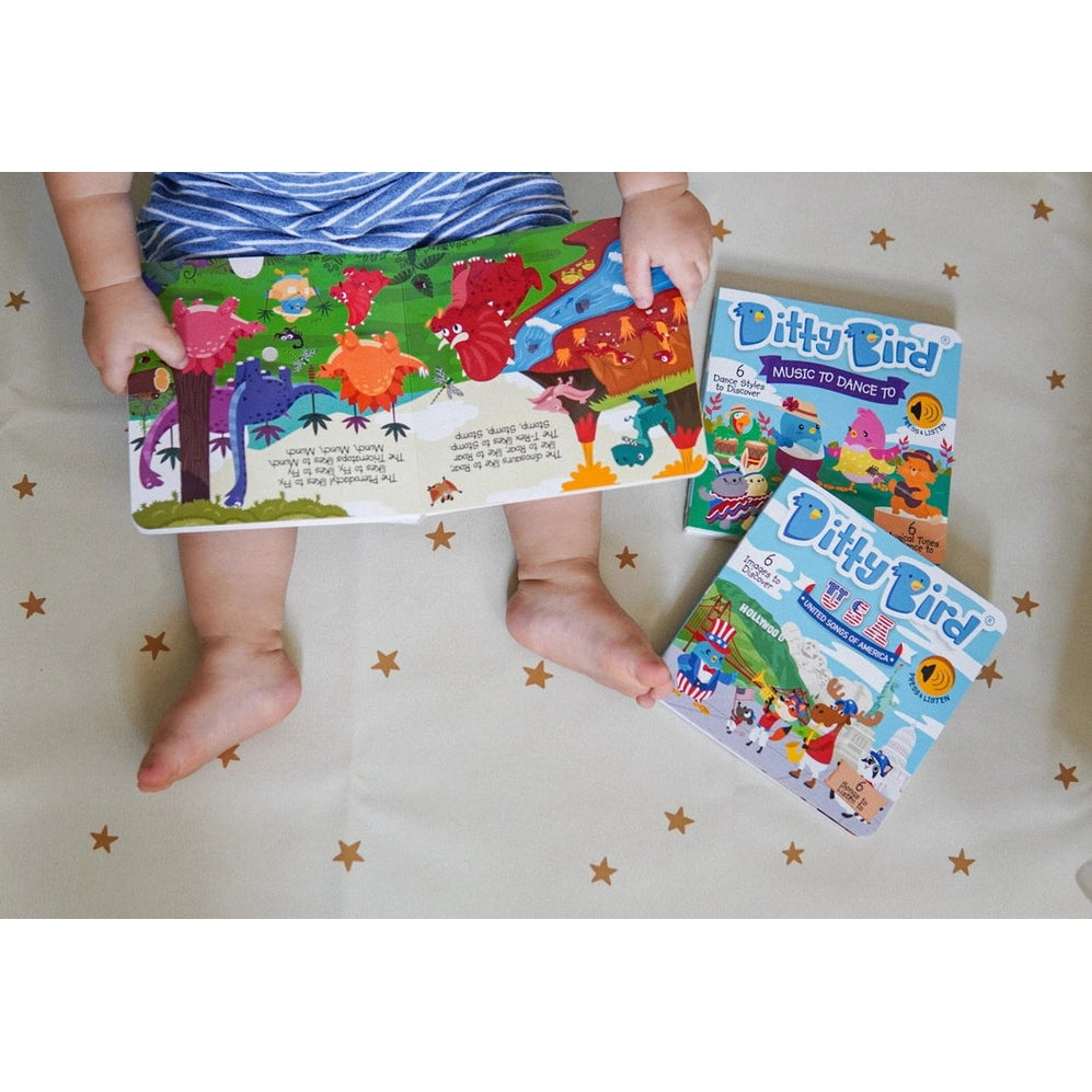 Ditty Bird Sound Book Dinosaur Sounds USB-C Rechargeable held by a toddler on a starry bedspread, with colorful dinosaur pages.
