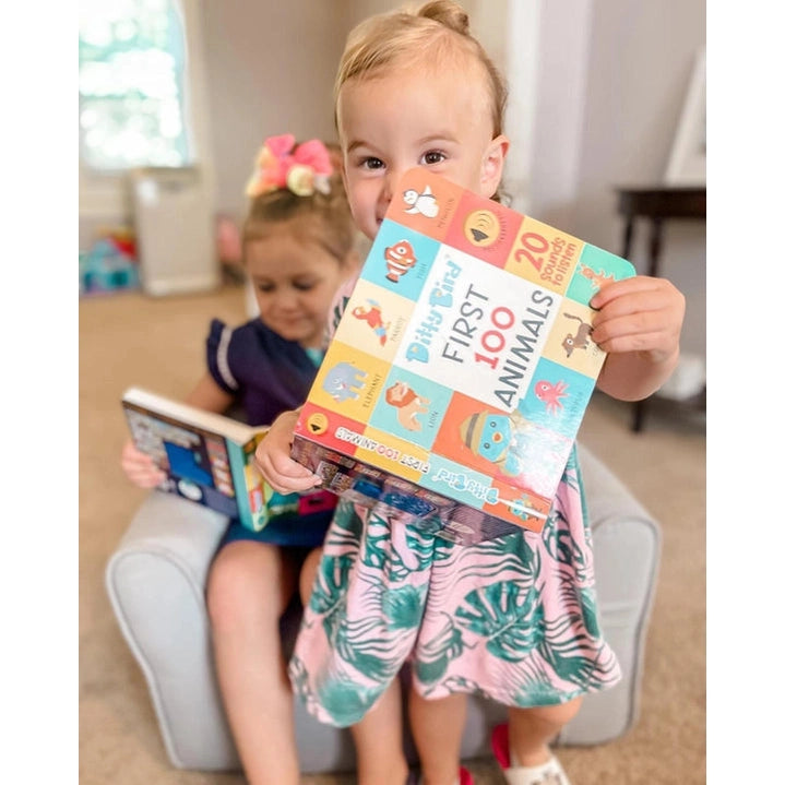 Ditty Bird Sound Book First 100 Animals USB-C Rechargeable held by a smiling toddler with colorful pages.