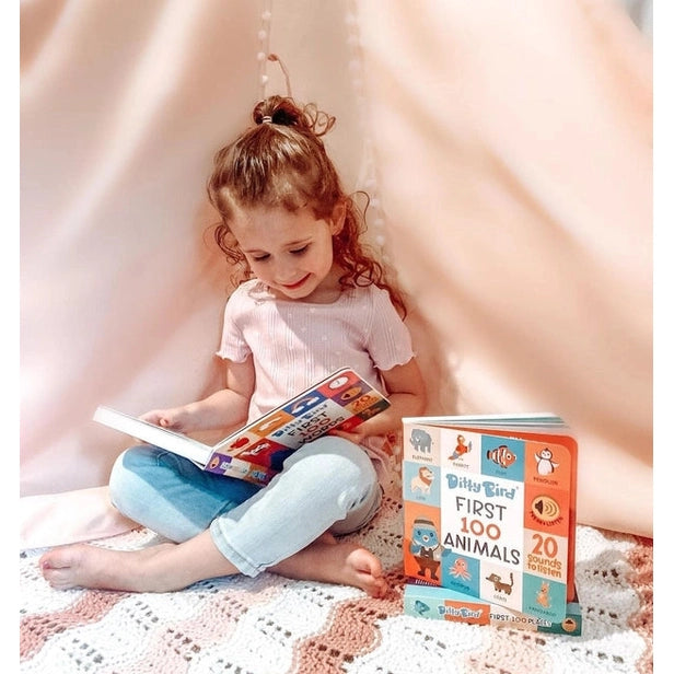 Ditty Bird Sound Book First 100 Words USB-C Rechargeable: a girl sits on a pink blanket, reading the colorful box advertising 20 sounds.