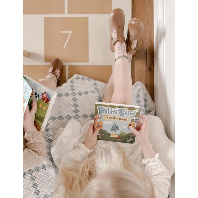 Ditty Bird Sound Book Funny Body Sounds USB-C Rechargeable; kid sits reading the colorful book on a cozy blanket.