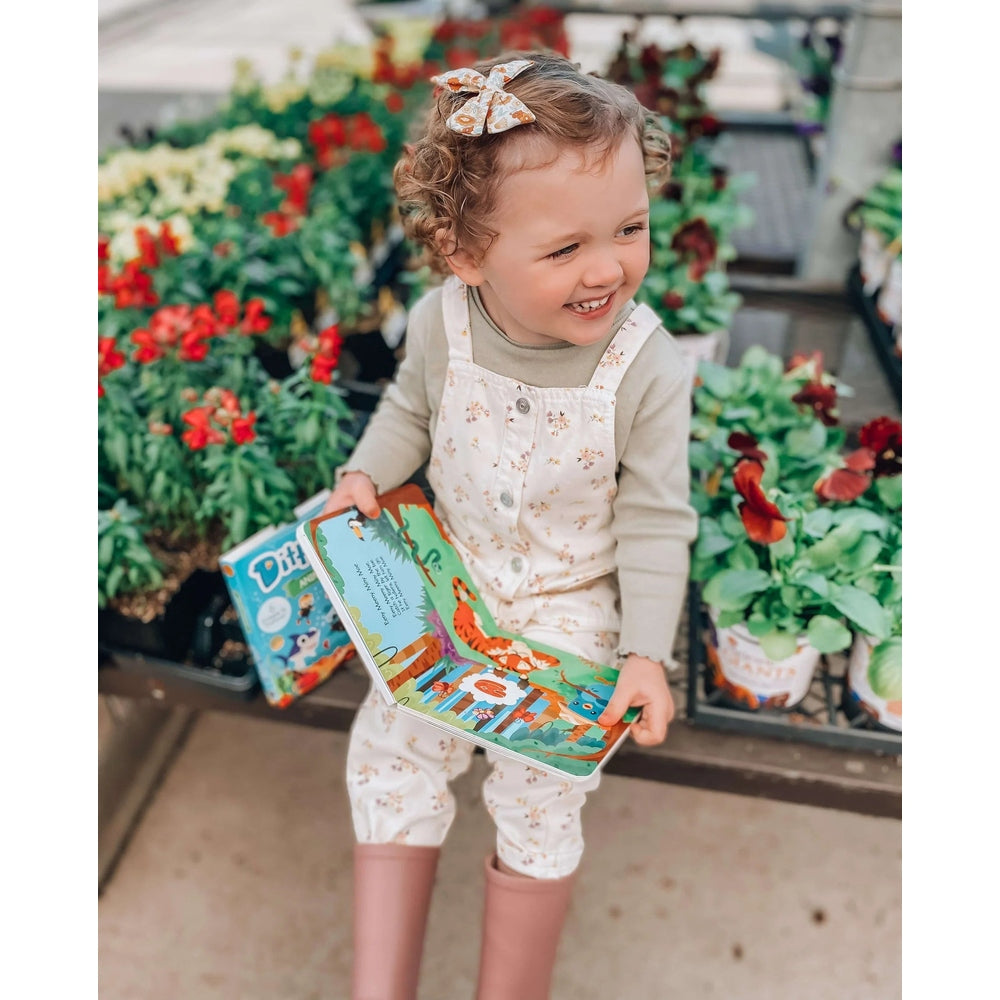 Ditty Bird sound book with colorful pages; toddler holds it outdoors among flowers