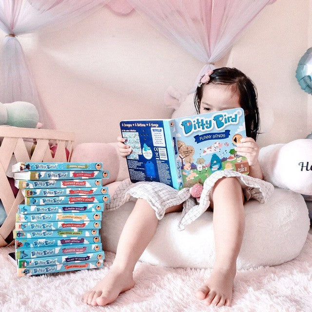 Ditty Bird Sound Book Funny Songs USB-C Rechargeable read by a girl, with a stack of Ditty Bird books beside.