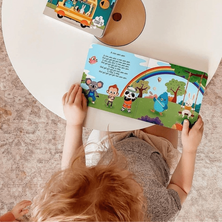 Ditty Bird Sound Book Funny Songs USB-C Rechargeable opened by a child at a round white table with colorful pages.