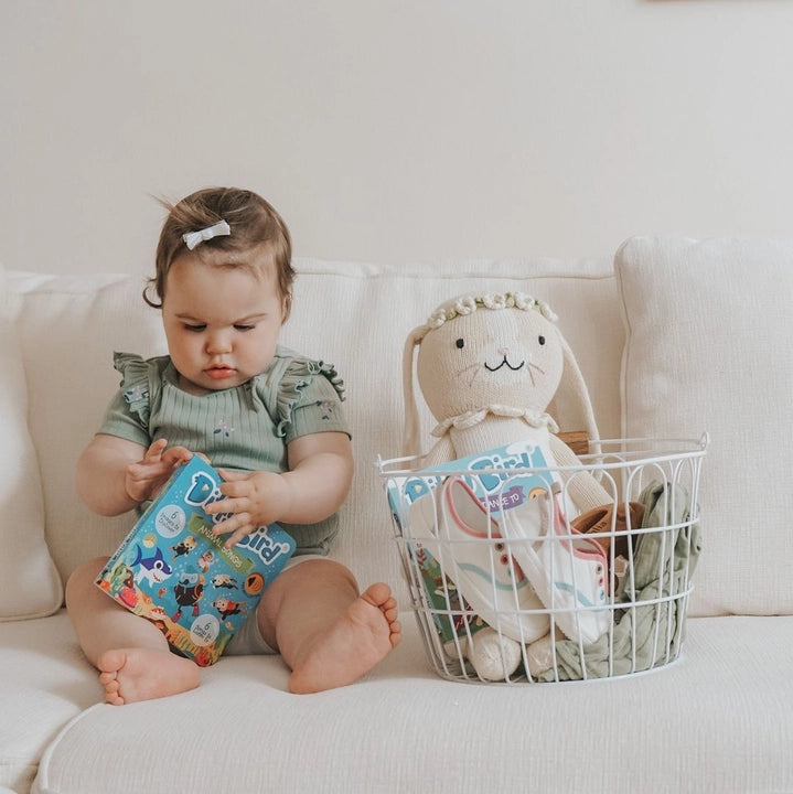 Ditty Bird Sound Book USB-C Rechargeable held by a baby on a white couch beside a plush bunny.