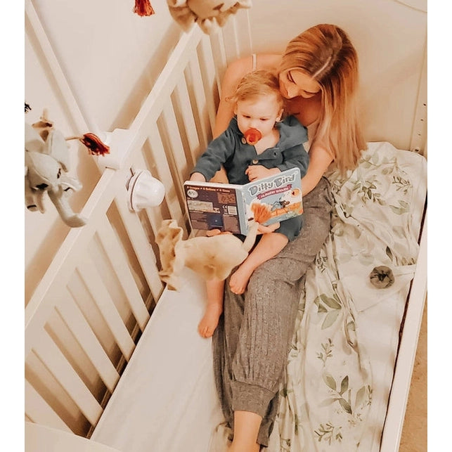 Ditty Bird Sound Book Nursery Rhymes USB-C Rechargeable being read by mom and toddler cuddled on a bed in a cozy nursery.