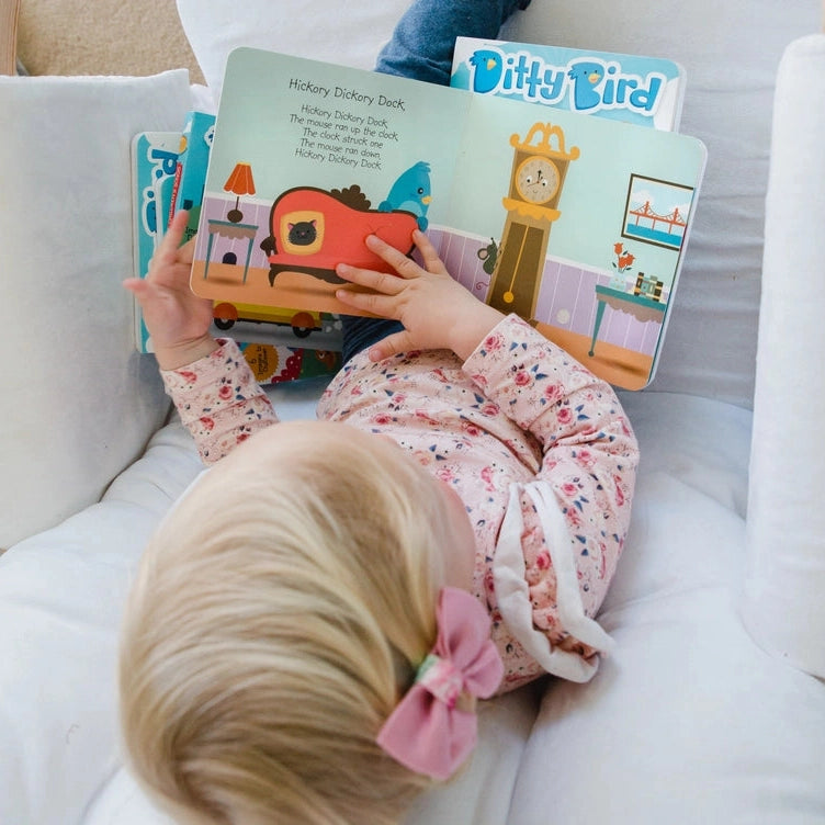 Ditty Bird Sound Book Nursery Rhymes USB-C Rechargeable being read by a toddler on a white couch.