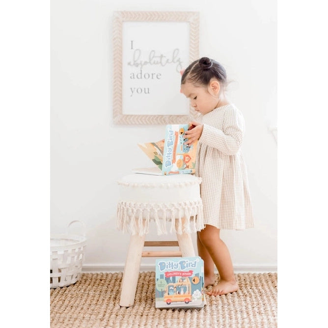 Ditty Bird Safari Animal Sounds USB-C rechargeable toy, a young girl reads a book at a fringed white side table.